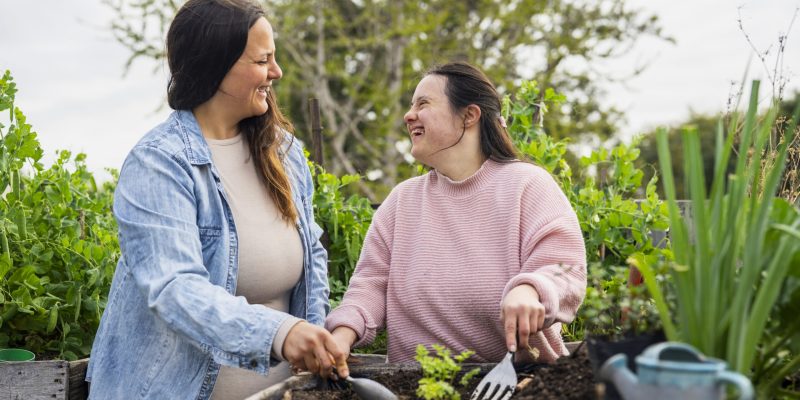 Portrait of young adult woman with down syndrome working on garden with mother during daytime