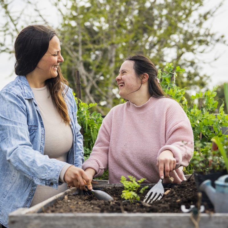 Portrait of young adult woman with down syndrome working on garden with mother during daytime