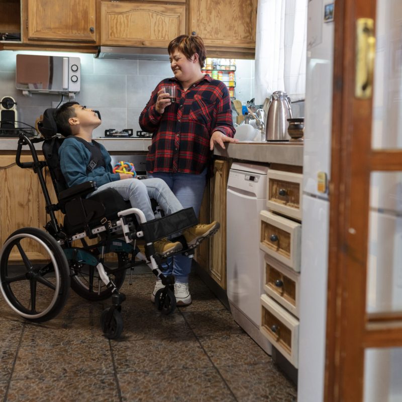 Latin mother drinking coffee in the kitchen with her disabled son. Concept of family, unconditional love and inclusion.